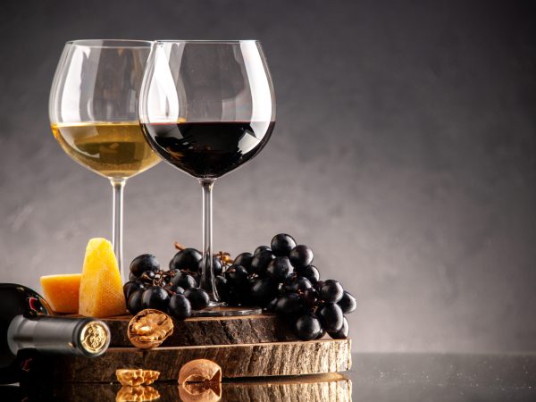 front-view-wine-glasses-fresh-grapes-walnuts-yellow-cheese-wood-board-overturned-bottle-dark-background