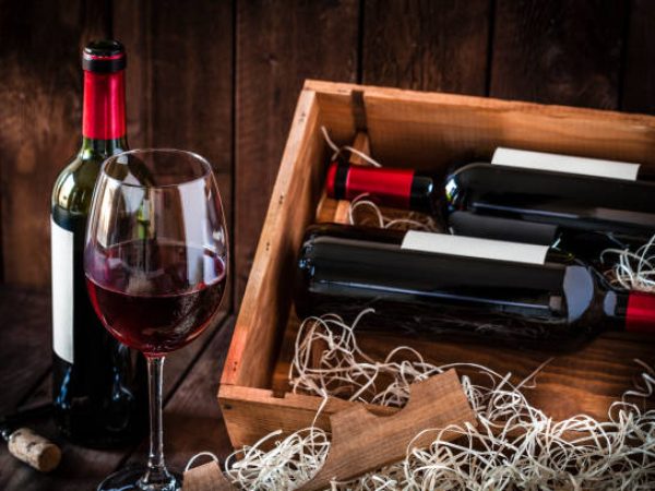 Front view of a wooden box with two wine bottles inside it and a third bottle out the box with a wineglass in front of it. A corkscrew with a cork is in besid the wineglass. Predominant color is brown. Low key DSRL studio photo taken with Canon EOS 5D Mk II and Canon EF 100mm f/2.8L Macro IS USM