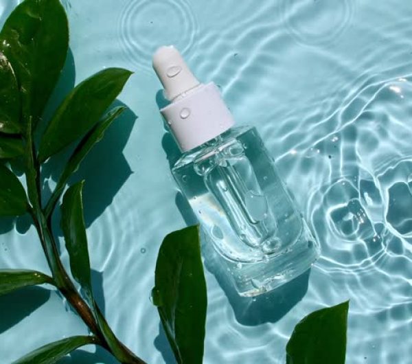 Glass cosmetic bottle with pipette lies on the surface of the water. Top view of water splash blue colored. Pure blue water with reflections sunlight. Sample of packaging for design, advertising.4k.
